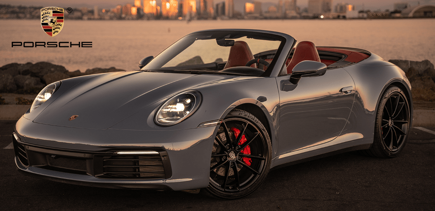 Silver convertible sports car parked by the water with city skyline in the background