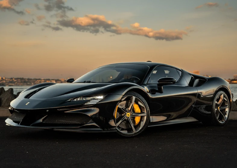 Black sports car with yellow brake calipers, parked by a waterfront at sunset