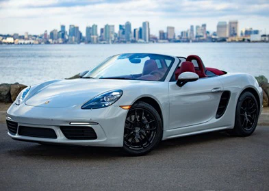 White convertible sports car parked near a body of water with a city skyline in the background