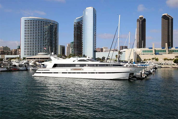A white yacht moored in a marina with tall buildings in the background