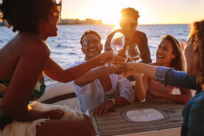 Group of five people on a boat raising glasses in a toast at sunset