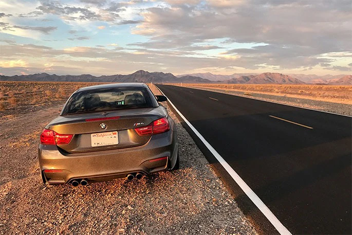 A gray car parked on the side of a desert road under a partially cloudy sky