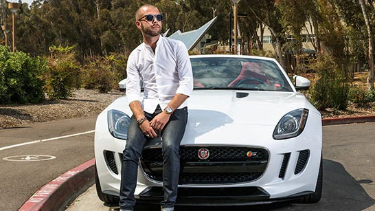 Man in a white shirt and sunglasses sits on a white sports car parked outdoors