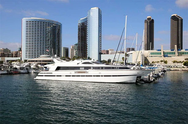 White yacht docked in a marina with tall buildings and a clear blue sky in the background