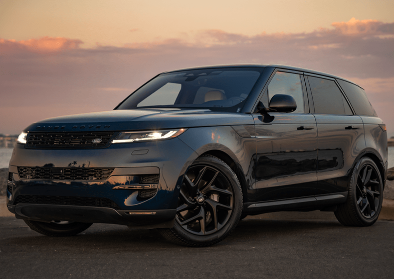 A dark blue SUV parked on a road with a sunset backdrop