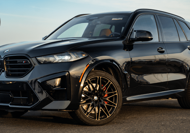 Black SUV parked near water, with a skyline in the background